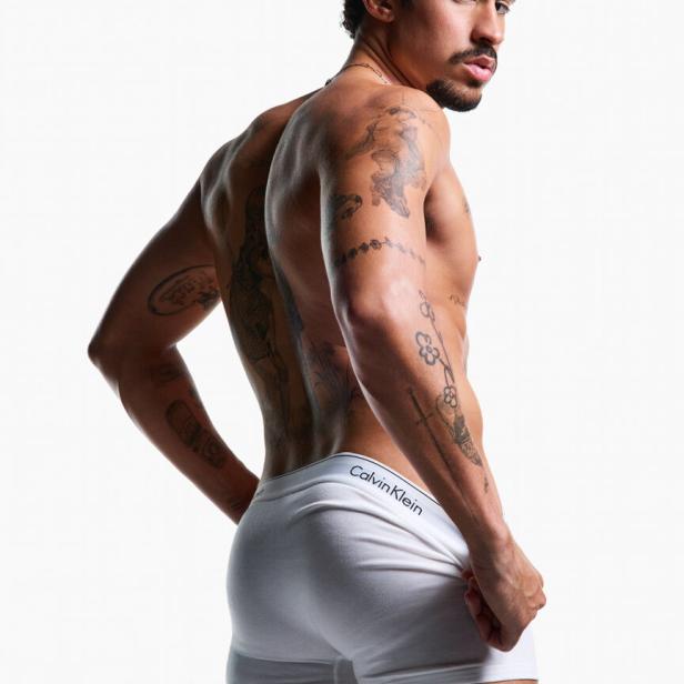 Ein Mann mit Tätowierungen trägt weiße Calvin Klein Unterwäsche.