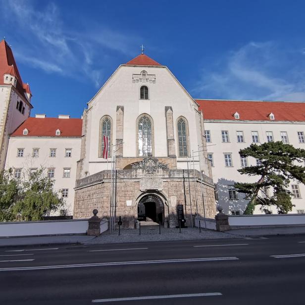 Große historische Klosteranlage mit rotem Dach und Torbogen vor blauem Himmel.
