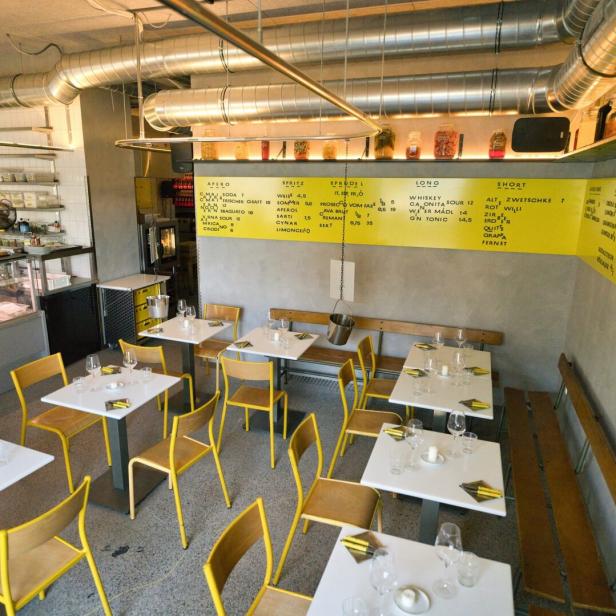 Einblick in ein Restaurant mit gelben Stühlen und Tischen mit Gedecken.