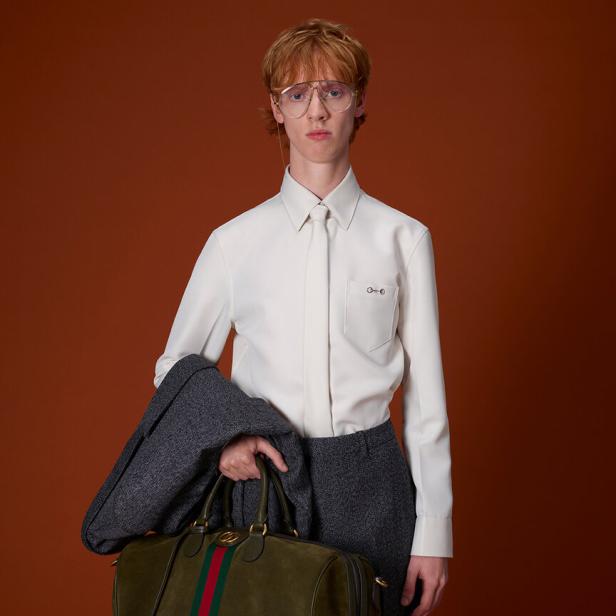 Ein Mann mit Brille hält eine grüne Gucci Reisetasche.