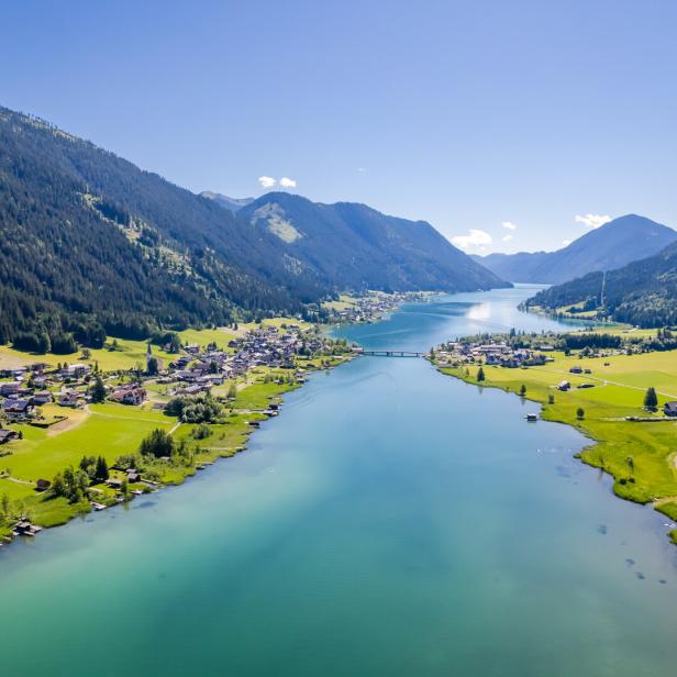 Luftaufnahme des Achensees, umgeben von Bergen und grünen Wiesen.