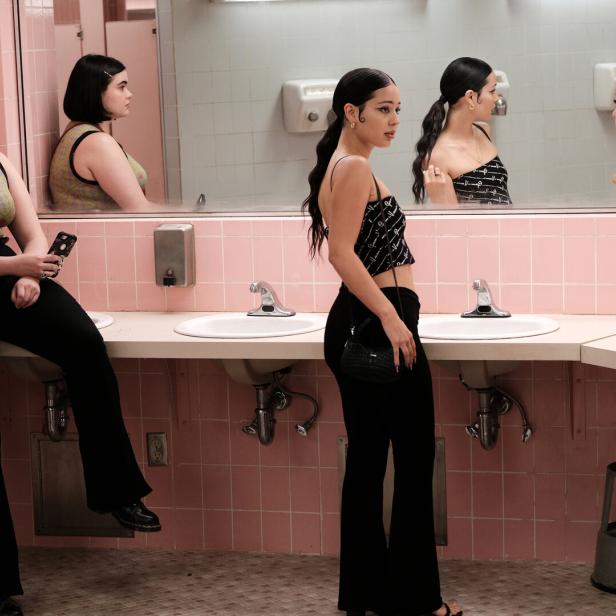 Drei junge Frauen stehen in einem Badezimmer mit rosa Fliesen vor einem Spiegel.