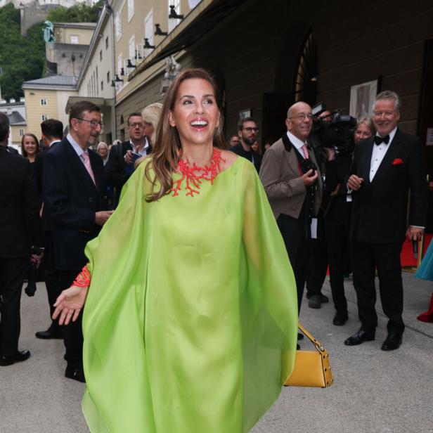 Eine Frau in einem hellgrünen Kleid und einer roten Korallenkette lächelt in die Kamera.