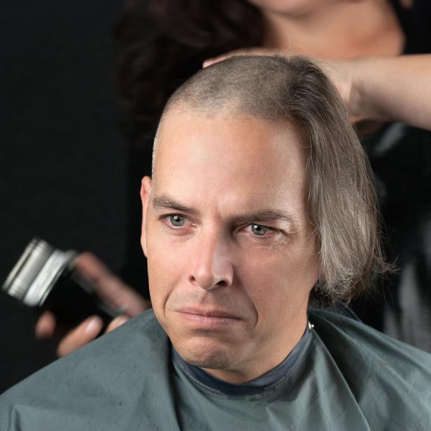 Ein trauriger Mann, dem für eine Krebs-Spendenaktion die langen Haare abrasiert werden.