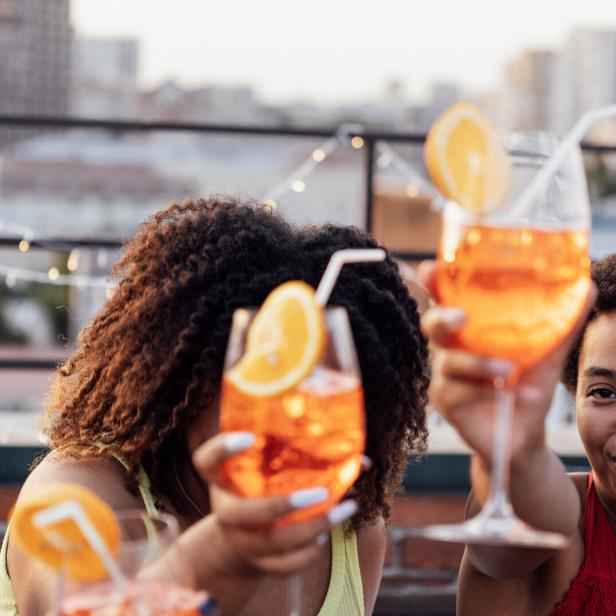 Freunde - offenbar in einer Rooftop-Bar - prosten einander mit Aperol Spritz zu.