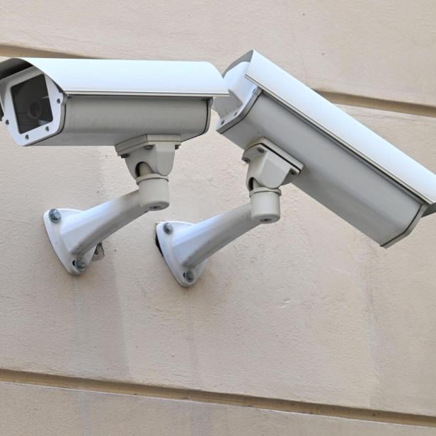 Zwei weiße Überwachungskameras sind an einer Wand montiert.
