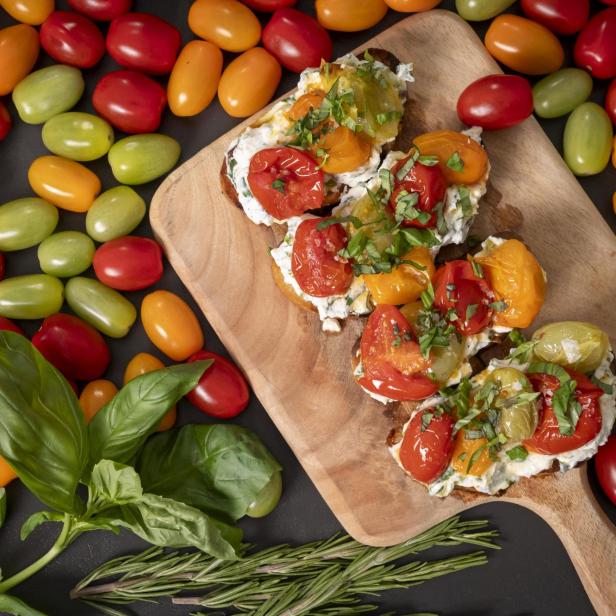 Ein Holzschneidebrett mit einer Ansammlung von Tomaten und frischen Kräutern.