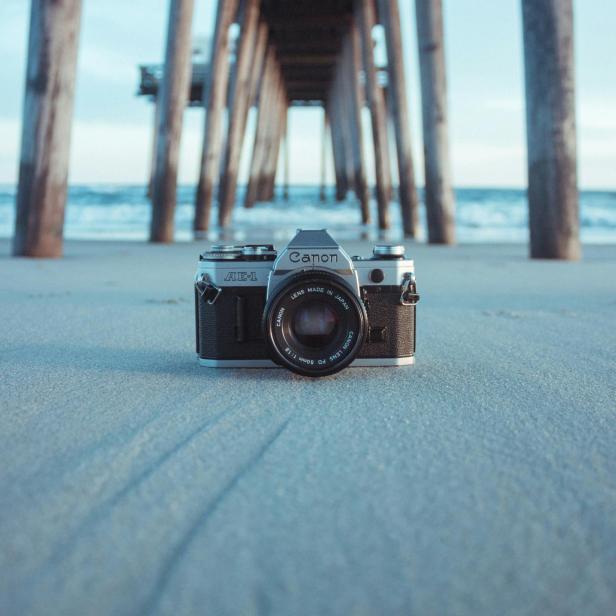 Kaamera platziert auf Sand, im Hintergrund ein Steg und das Meer.