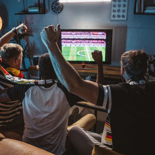 Fußballfans sitzen gemeinsam vor dem Fernseher und jubeln.
