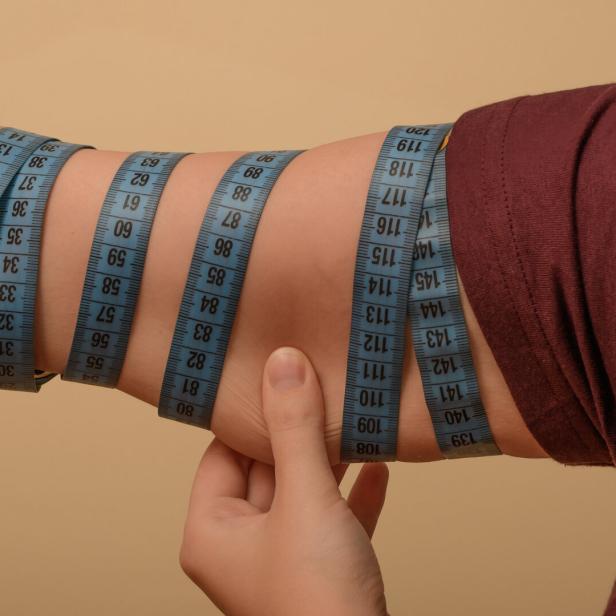Eine Frau misst ihren Oberarmumfang mit einem Maßband.