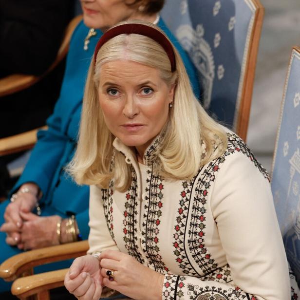 Mette-Marit sitzt in einem bestickten weißen Kleid.