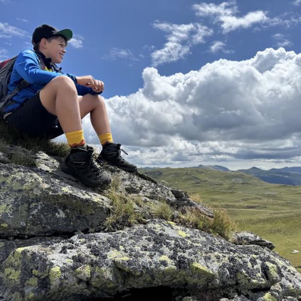 Kind sitzt auf einem Felsen und schaut in die Landschaft.
