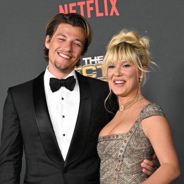 Schauspielerin Millie Bobby Brown und ihr Mann Jake Bongiovi lächeln in die Kamera. Sie tragen elegante Abendkleidung.