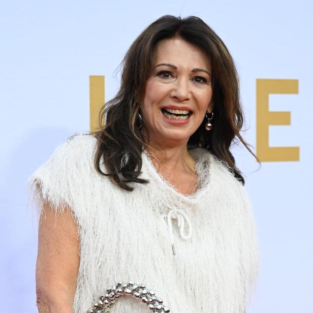 Eine Frau mit weißem Kleid und silberner Handtasche lächelt.