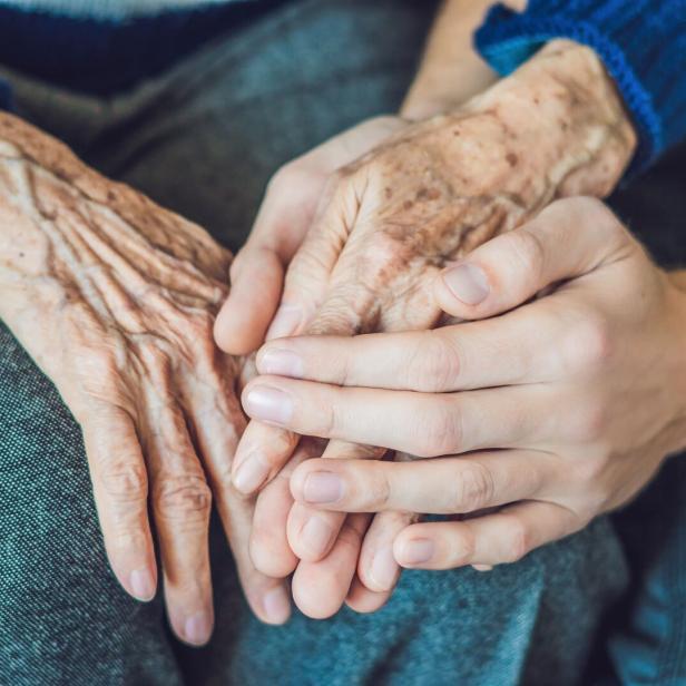 Eine junge Hand berührt die Hände einer alten Person.