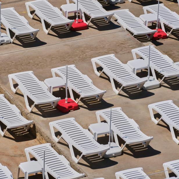 Weiße Sonnenliegen stehen aneinandergereiht am Strand