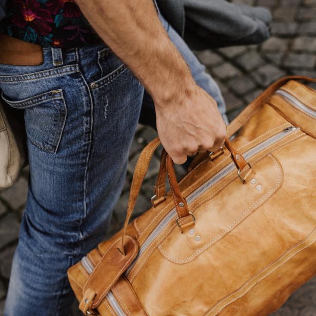 Ein Mann trägt eine braune Ledertasche und eine Stofftasche.