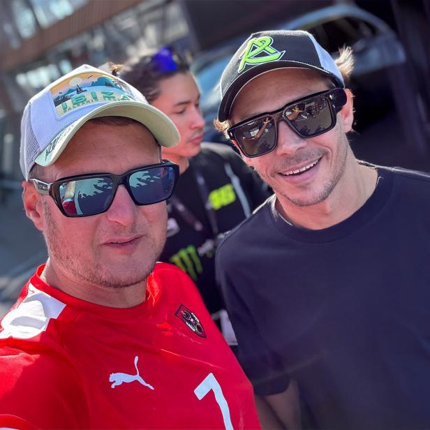 Zwei Männer mit Sonnenbrillen und Kappe machen ein Selfie und lachen in die Kamera.