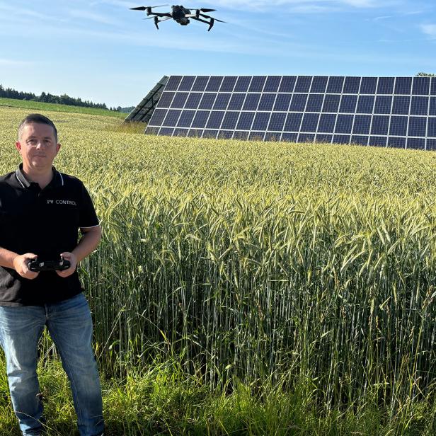 Ein Mann steht mit einem Controller vor einem Feld, im Hintergrund Solarpanele.