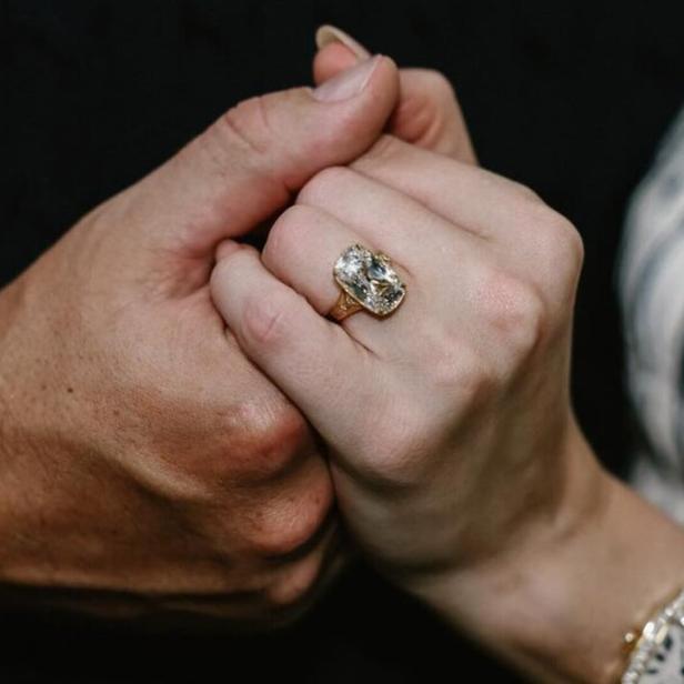 Ein Paar hält Händchen, wobei ein großer Diamantring an der Hand der Frau zu sehen ist.
