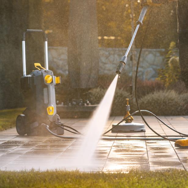 Eine Person mit gelben Gummistiefeln reinigt Terrassenplatten mit einem Kärcher.