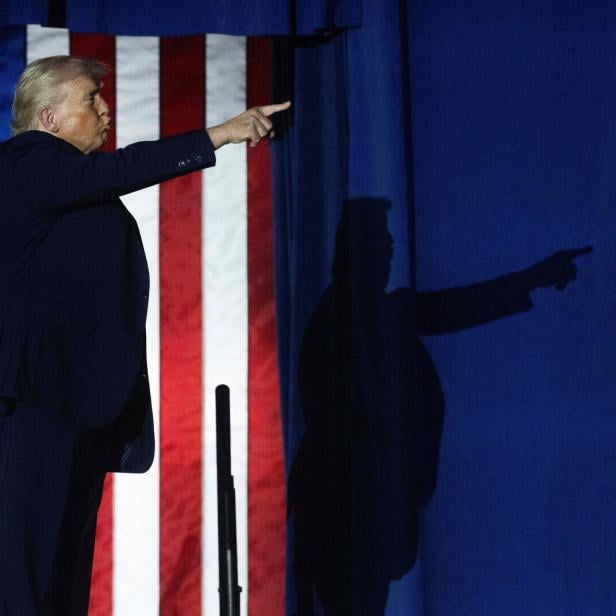Trump vor US-Flagge, sein Schatten im Hintergrund