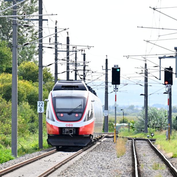 ÖBB-Zug fährt auf elektrifizierter Strecke mit Oberleitungen und Signalen durch eine grüne Landschaft.