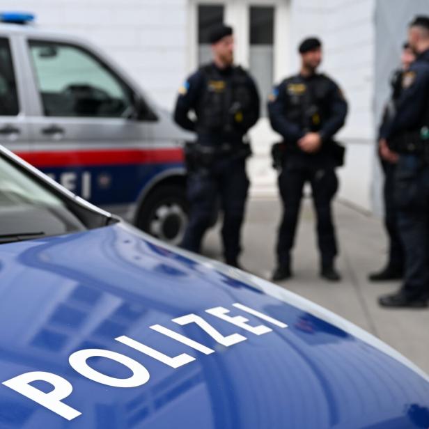 Polizeiautos, drei Polizisten im Hintergrund.