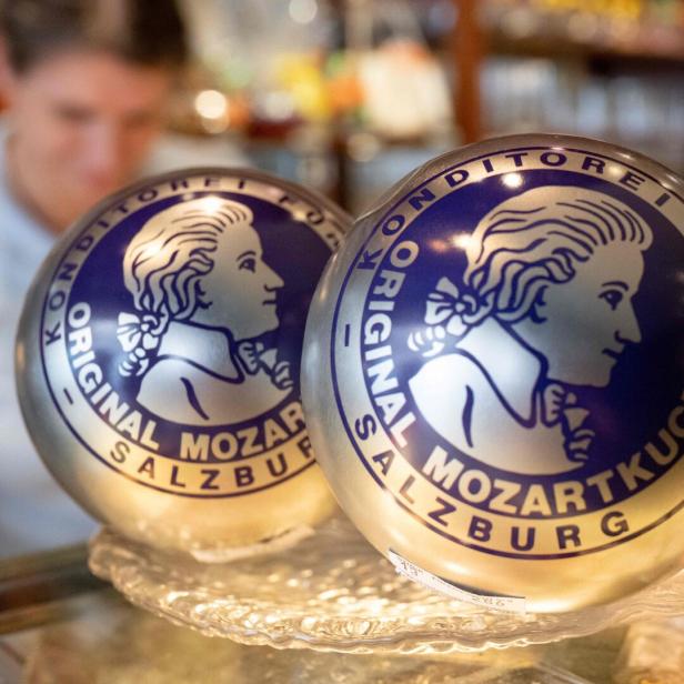 Zwei Kugeln mit Mozartkugel-Logo in einer Vitrine, im Hintergrund eine unscharfe Person.