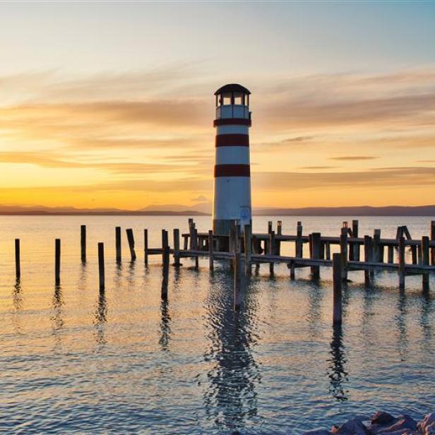 Ein rot-weißer Leuchtturm am Ufer des Neusiedlersees im Sonnenuntergang.