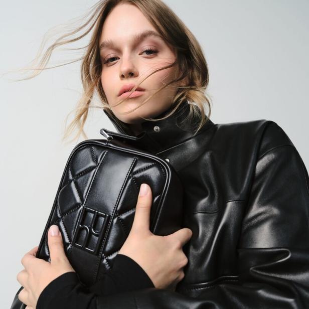 Eine Frau mit Lederjacke hält eine schwarze, gesteppte Handtasche.