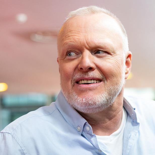 Stefan Raab schaut zur Seite. Er trägt ein hellblaues Hemd und ein weißes Shirt darunter.