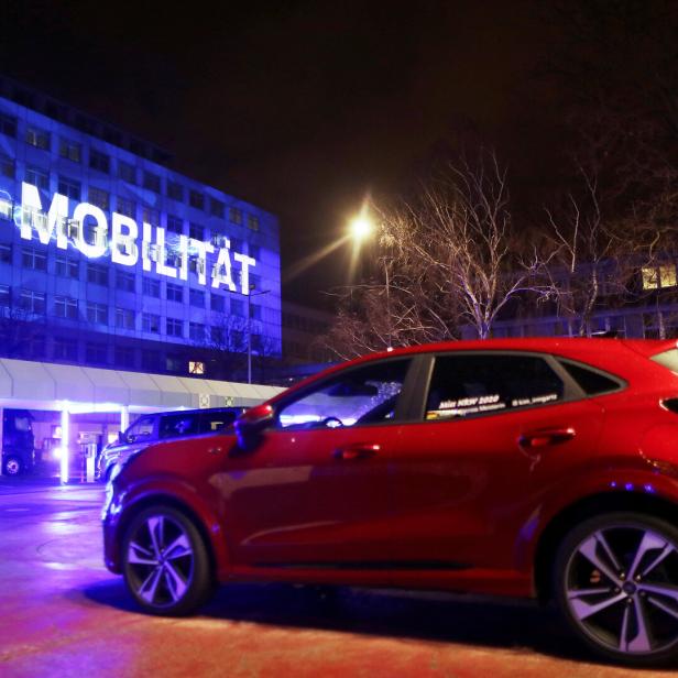 Elektroauto vor einem Gebäude mit darauf projiziertem E-Mobilität Schriftzug.