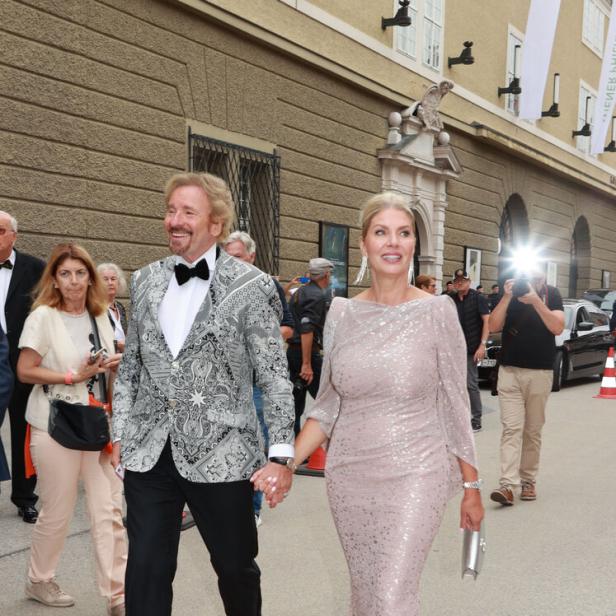 Thomas Gottschalk im gemusterten Sakko und Karina Mroß im Paillettenkleid gehen händchenhaltend an einem Gebäude entlang.
