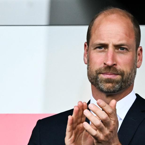 Prinz William klatscht in einem dunklen Anzug vor einem hellen Hintergrund.