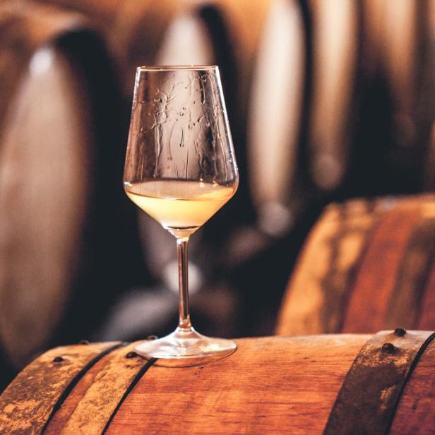 Ein Glas Weißwein steht auf einem Holzfass im Weinkeller.