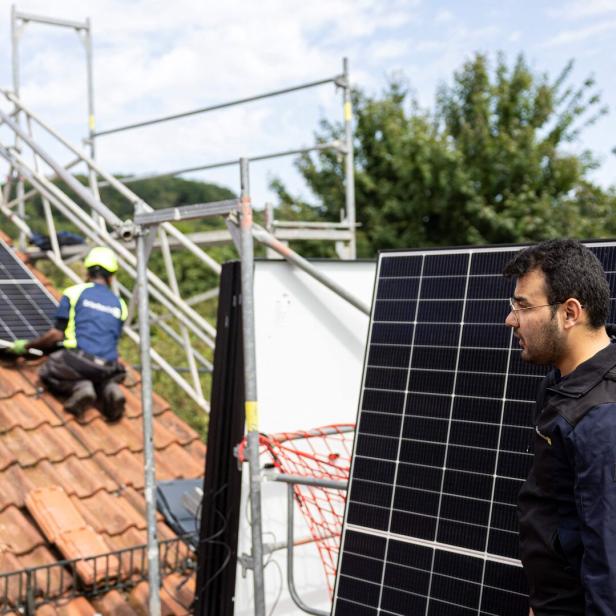 Arbeiter installieren eine PV-Anlage auf dem Dach eines Einfamilienhauses.