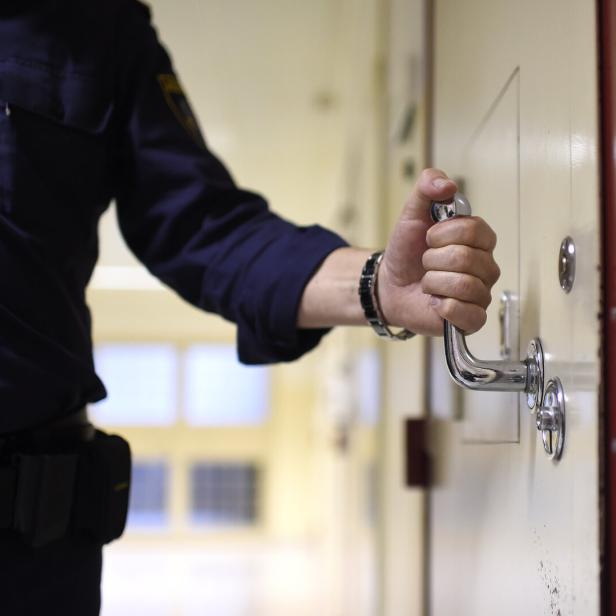 Eine Person in Uniform öffnet mit der rechten Hand eine schwere Tür mit Metallgriff in einem Flur.