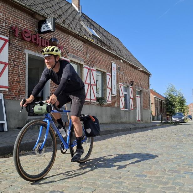 Ein Radfahrer fährt auf einer Kopfsteinpflasterstraße an einem Backsteingebäude vorbei.