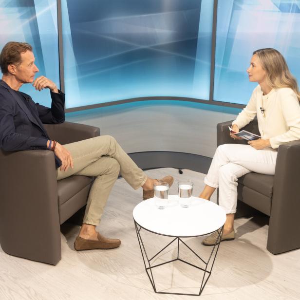 Wolfgang Fojtl sitzt im TV-Studio auf einem braunen Couch-Sessel gegenüber von Moderatorin und Journalistin Jennifer Corazza