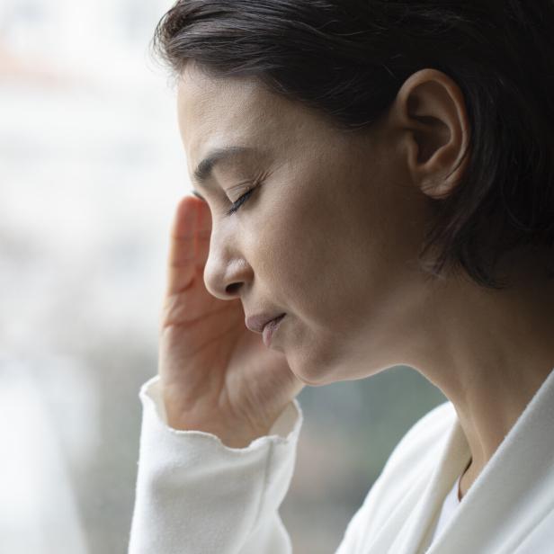 Frau mit geschlossenen Augen hält sich die Schläfe und wirkt nachdenklich oder erschöpft.