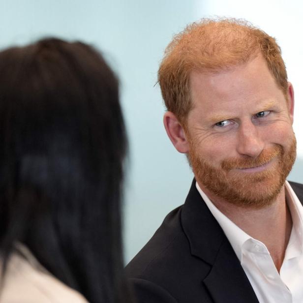 Prinz Harry blickt mit einem Lächeln auf eine Person mit dunklen Haaren.