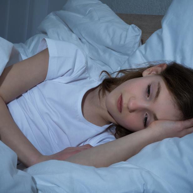 Das Bild zeigt eine junge Frau mit Schlafproblemen wach im Bett. 