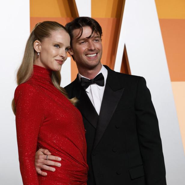 Patrick Schwarzenegger und Abby Champion posieren elegant, sie trägt ein glitzerndes rotes Kleid, er einen schwarzen Smoking mit Fliege, beide lächeln.