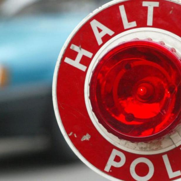 Eine rote Polizeikelle mit der Aufschrift „Halt Polizei“ wird vor einem unscharfen Auto gezeigt.