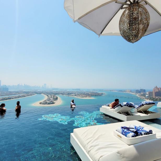Menschen entspannen am Infinity-Pool mit Blick auf die Skyline von Dubai.