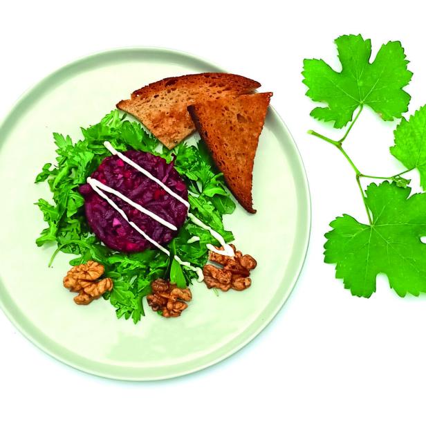 Ein Teller mit Rote-Bete-Tatar, Salat, Toast und Walnüssen, garniert mit Weinblättern.
