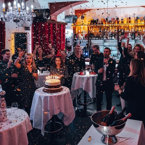 Eine Gruppe von Menschen feiert in einem Restaurant einen Geburtstag mit Kuchen und fröhlicher Stimmung.