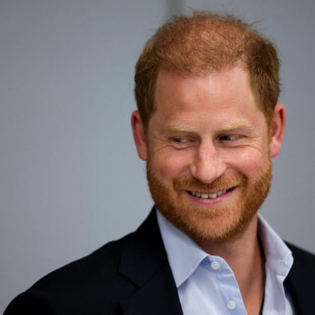 Prinz Harry lächelt mit Bart und hellblauem Hemd zur Seite.