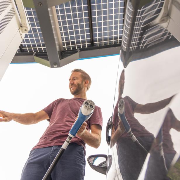Man Initiating Electric Vehicle Charging Under Solar Canopy